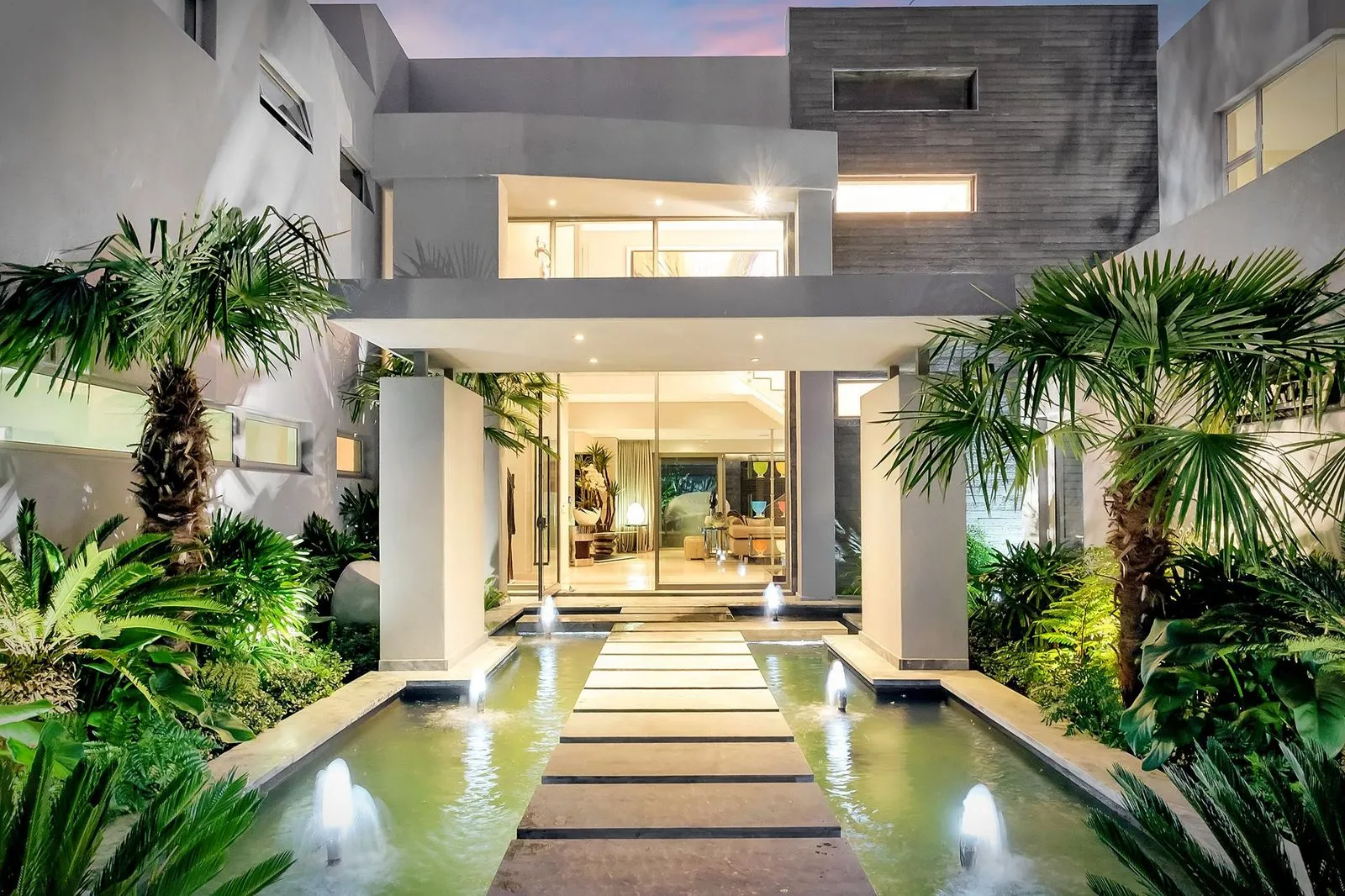 Entrance of a modern residence with a lit water feature and tropical planting